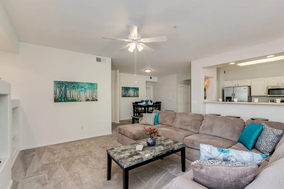 An inviting open-plan living and dining space, with a sofa, coffee table, artwork, and a visible dining area in the background. The layout encourages both relaxation and social gatherings, perfect for families coming together for meals or evening downtime.