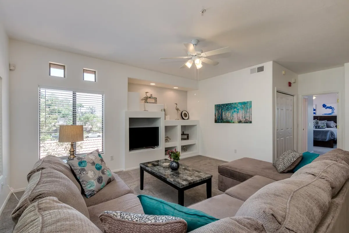 A spacious living room featuring a plush sectional sofa, decorative artwork, a central coffee table, and large windows that fill the space with natural light. The inviting arrangement is perfect for both relaxing with family and entertaining guests.
