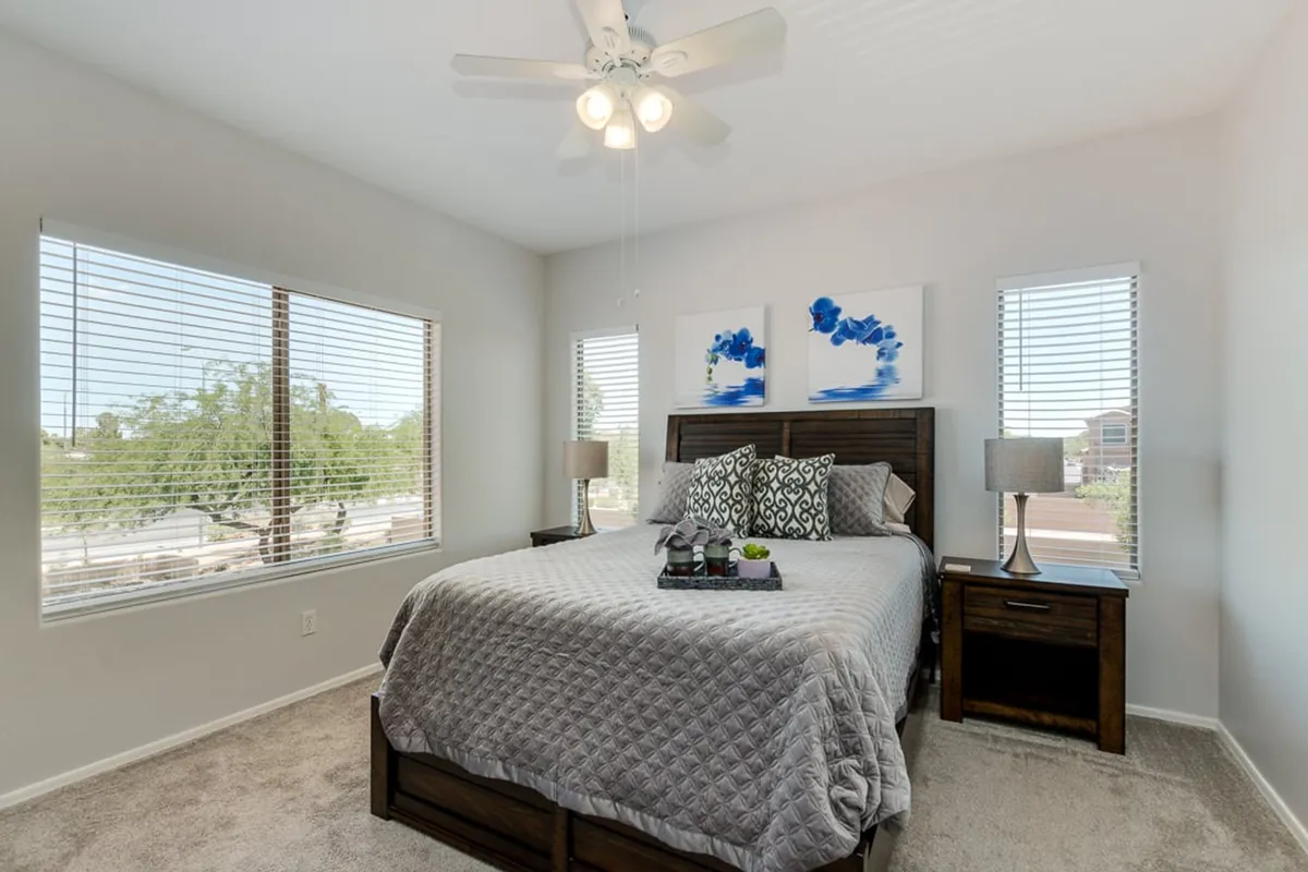 A serene bedroom featuring a large, inviting bed with decorative pillows, warm lighting from stylish nightstands, and calming artwork above the headboard. The mood is tranquil and cozy, ideal for unwinding after a long day.
