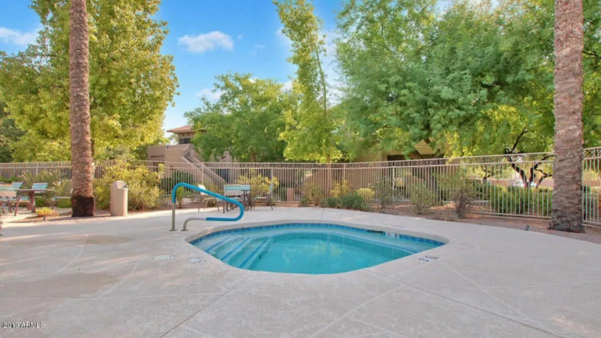 Another view of the community swimming pool, this time emphasizing the tranquil water, surrounding greenery, and multiple lounge chairs. The pool area appears spacious and serene, perfect for both social gatherings and quiet mornings by the water.