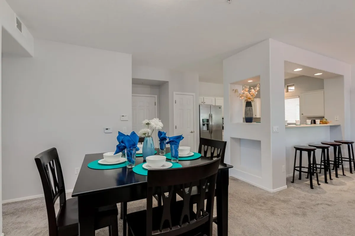 A dining area set for a meal with a stylish dining table, blue table settings, and a kitchen pass-through, highlighting the seamless flow between kitchen and dining spaces. The setup is ideal for both intimate family dinners and festive gatherings.
