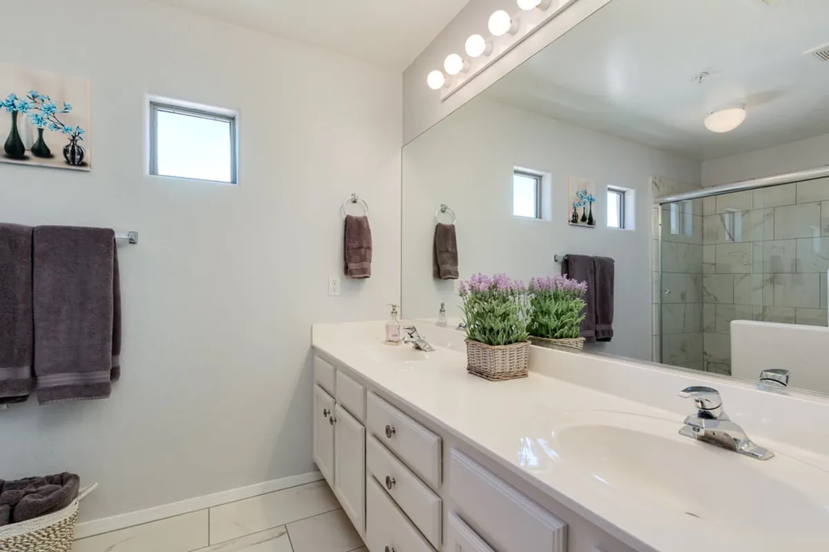 A bright and modern ensuite bathroom featuring a double sink vanity, a large mirror, a shower enclosure, and a tasteful floral arrangement. The space reflects both style and privacy, perfect for morning routines or evening relaxation.