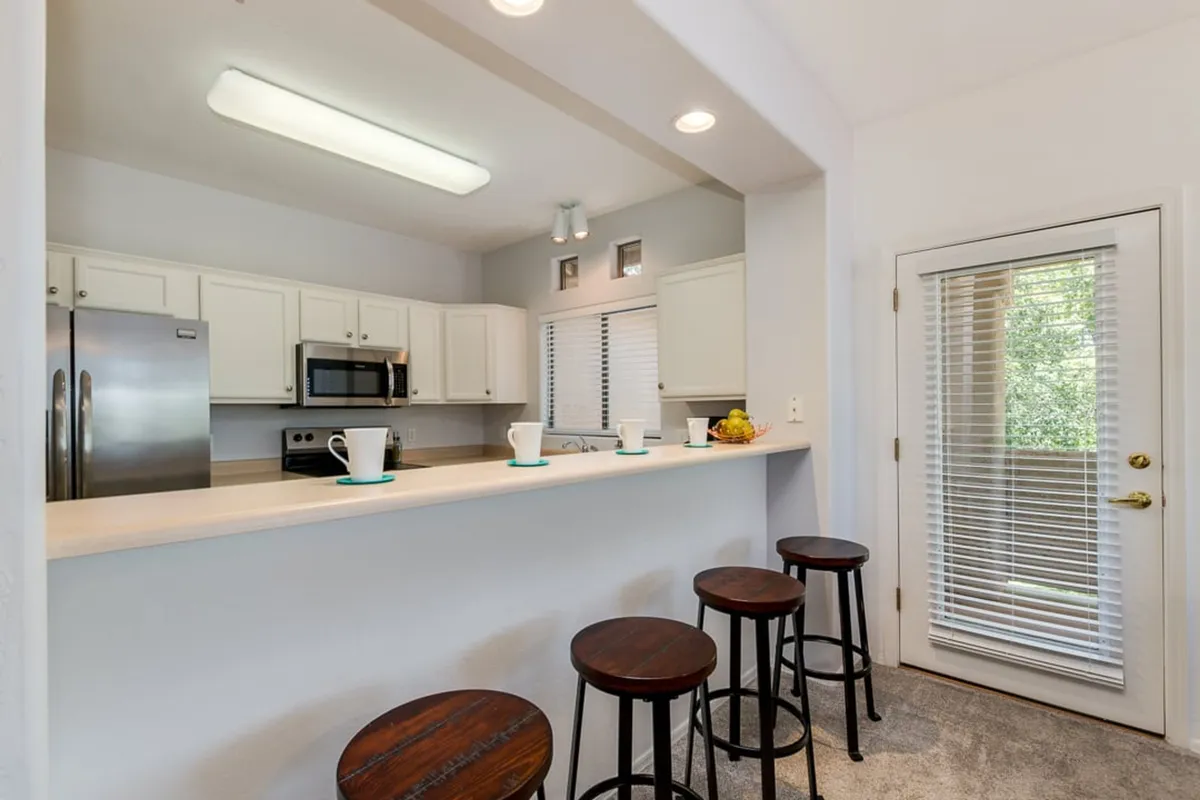 A modern kitchen with a large island and bar stools, complemented by sleek appliances and a window offering an inviting view. The open layout is perfect for casual dining and entertaining, reflecting the option for family meals together after a day out.