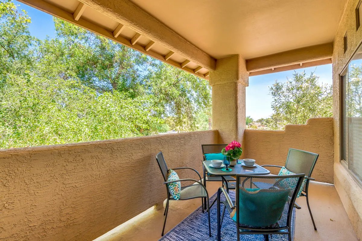 This image captures an exterior balcony space featuring a charming table setting with decorative cushions, surrounded by lush greenery. The setup overlooks green views and is ideal for outdoor meals or relaxing with a beverage, visually emphasizing the balcony’s role as a private retreat.